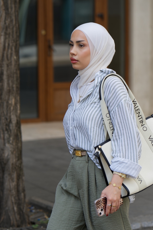 1 - Person styling a blue and white striped button-down shirt with high-waisted olive green trousers and a white Valentino shoulder bag